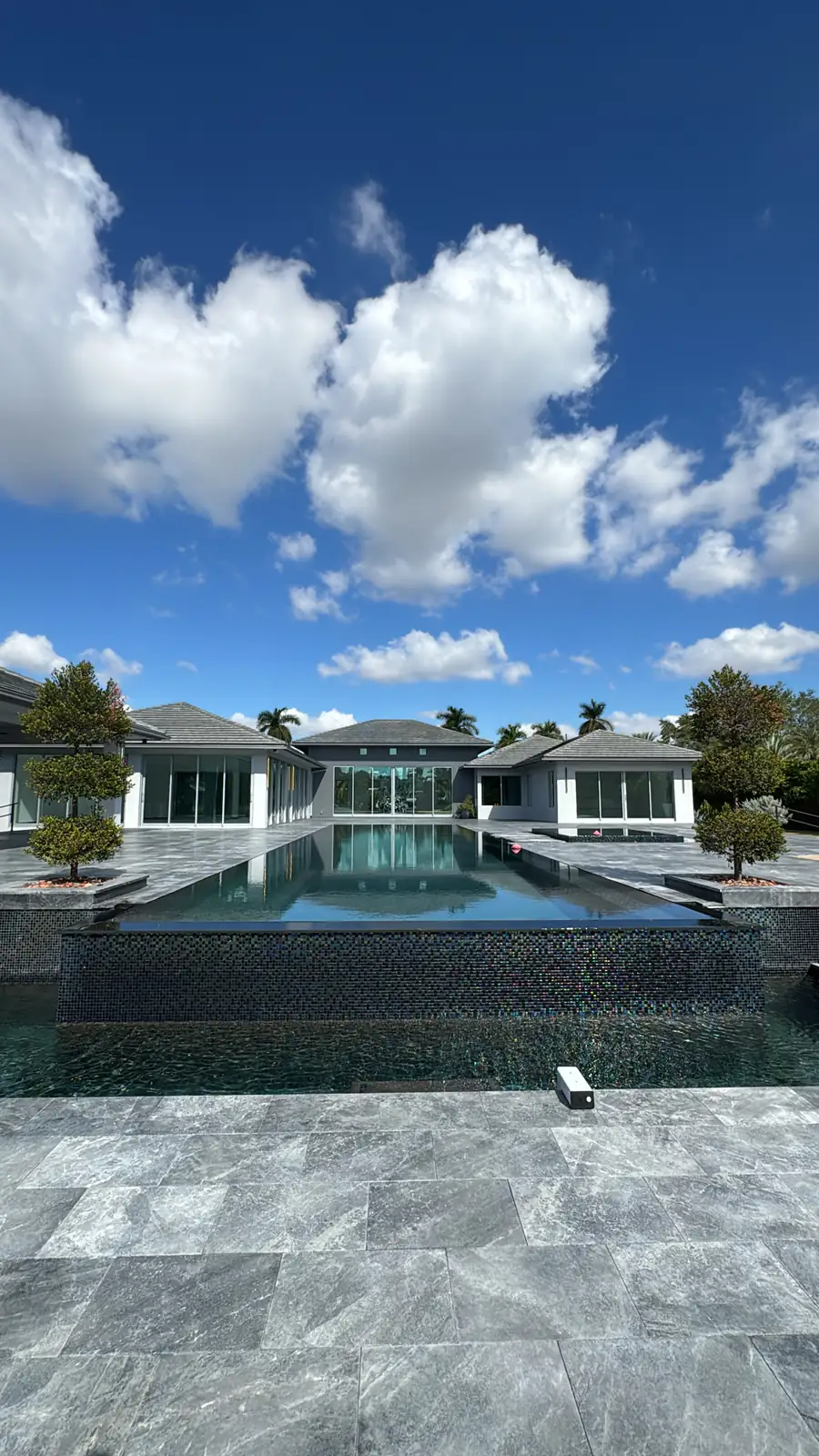 Una casa moderna de una planta detrás de una piscina infinita y una terraza de piedra