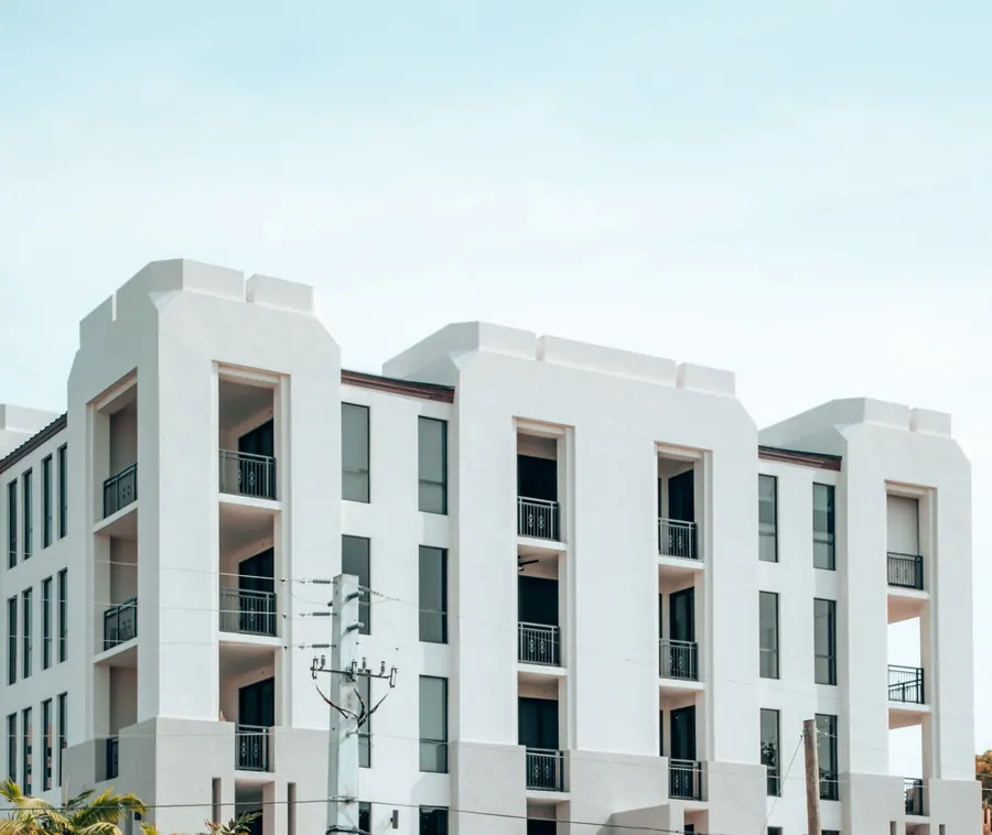 A low white residential building in Coral Gables with recessed balconies, palms and a utility pole in front