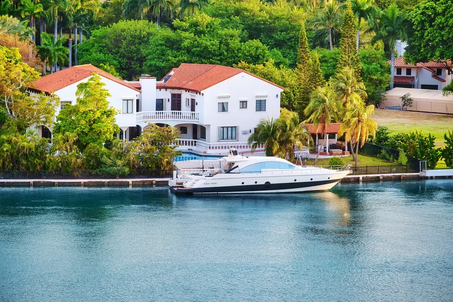 A white stucco waterfront estate with a barrel-tile roof and balustraded terrace, a motor yacht moored against its seawall
