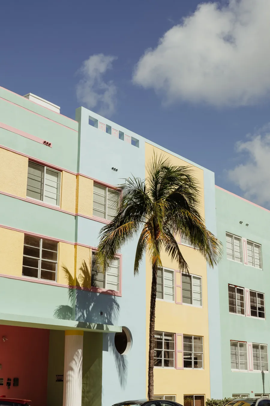 A pastel Art Deco apartment building in mint, yellow and pink, a coconut palm in front of it